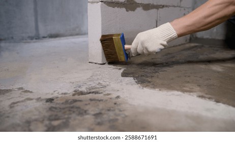 Construction worker applying a waterproofing membrane to a concrete floor using a brush, ensuring long-lasting protection against moisture