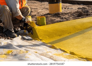 Construction worker applying yellow marking paint to concrete curb edge at roadwork site