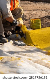 Construction worker applying yellow marking paint to concrete curb edge at roadwork site