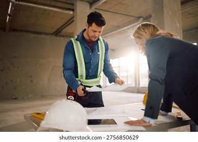 Construction worker and architect analyzing project plans at building site.