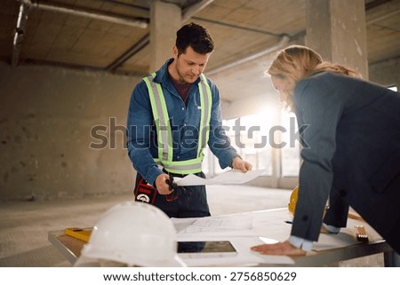 Construction worker and architect analyzing project plans at building site.