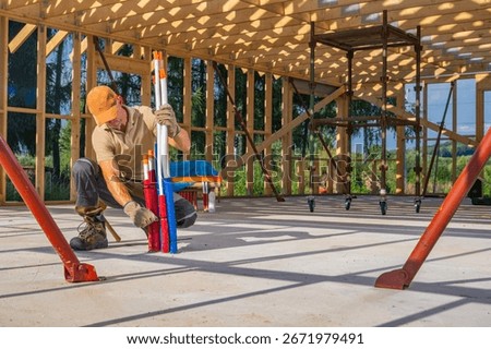 A construction worker arranges colorful support poles in an unfinished structure. Natural light streams through the framework, showcasing the construction progress.