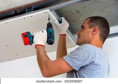 Construction worker assemble a suspended ceiling with drywall and fixing the drywall to the ceiling metal frame with screwdriver. Renovation, construction and do it yourself DIY concept.