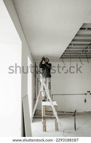 Construction worker assemble a suspended ceiling with drywall and fixing the drywall to the ceiling metal frame with screwdriver. Renovation, construction and do it yourself DIY concept