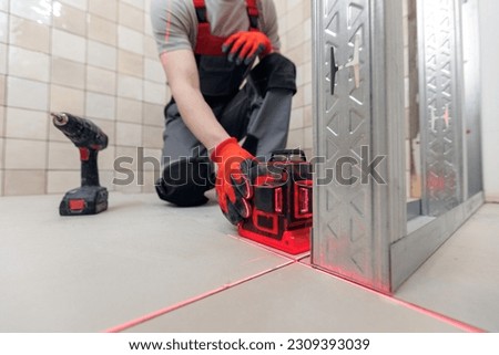 Construction worker assemble wall with attach to metal frame with laser level and screwdriver for drywall in bathroom.