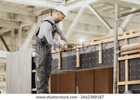 Construction worker assembling prefabricated modular building using electric screwdriver in large factory