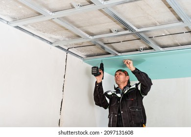 Construction Worker Assembly Suspended Ceiling With Drywall And Fixing The Drywall To The Ceiling Metal Frame With Screwdriver.