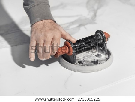 Construction worker attaching vacuum suction cup lifter to large format tile surface. Close view of handы positioning lifting tool on ceramic slab during tile installation process