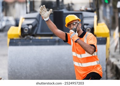 A construction worker in a bright safety vest and hard hat is signaling for vehicles to stop while overseeing roadwork in a busy urban area. - Powered by Shutterstock