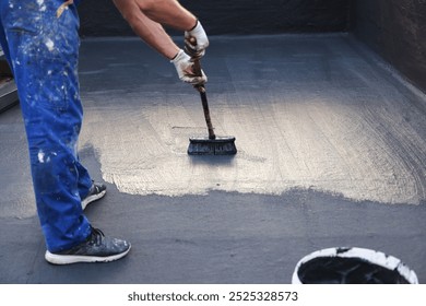 Construction worker with brush applying waterproofing layer coating on a building roof