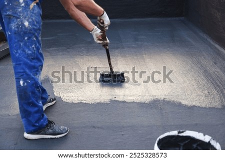 Construction worker with brush applying waterproofing layer coating on a building roof 