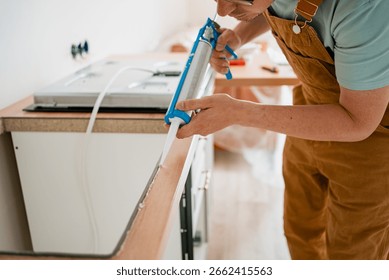 Construction worker carefully applying silicone sealant to seal countertop in kitchen, ensuring protection against water damage and enhancing kitchen hygiene