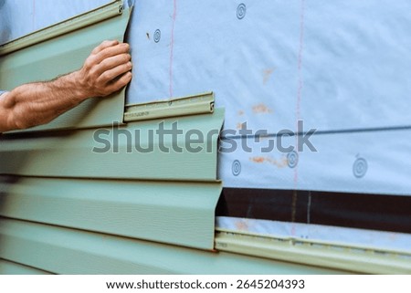 Construction worker carefully fits section of green PVC siding onto wall during home improvement task.