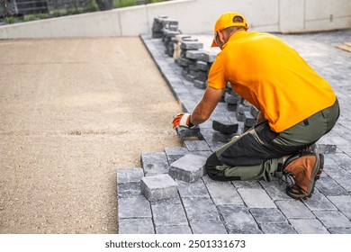 A construction worker carefully positions cobblestones to create a new patio in a residential yard under bright sunlight.