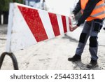 A construction worker carefully positions a safety barrier on a bustling city street, ensuring safety precautions are in place for pedestrians and vehicles during daytime.