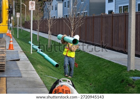 Construction worker carrying section of new 8 inch sewer line pipe for installation as part of new public sewer system infrastructure installation for new housing development
