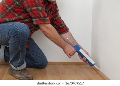 Construction Worker Caulking  Batten Of Laminate Floor Using Silicone Glue In A Cartridge, Closeup Of Hands, Home Renovation