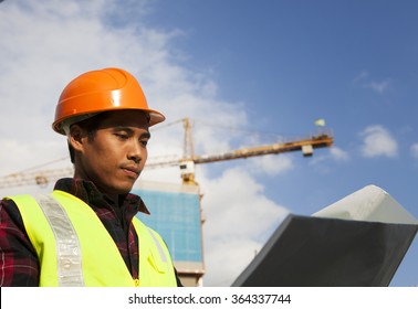 Construction worker checking blueprint paper document wear helmet with crane in background