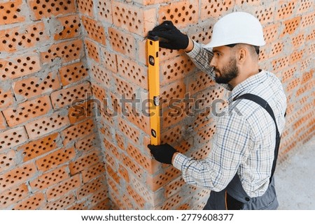 Construction worker checking brick wall with a spirit level, ensuring precision and quality in building work