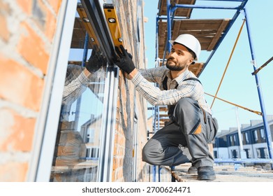 Construction worker checking window frame alignment with a spirit level on a building site. New house construction
