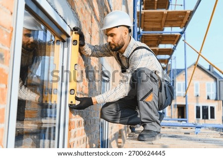 Construction worker checking window installation for levelness while standing on scaffolding. Building new house