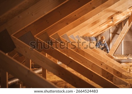 A construction worker checks insulation materials in a wooden attic space with exposed beams and a neat arrangement of structural elements.