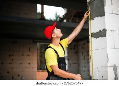 Construction worker checks vertical height of window opening, site measurements for installation, planning wall partitions, building renovation tasks.