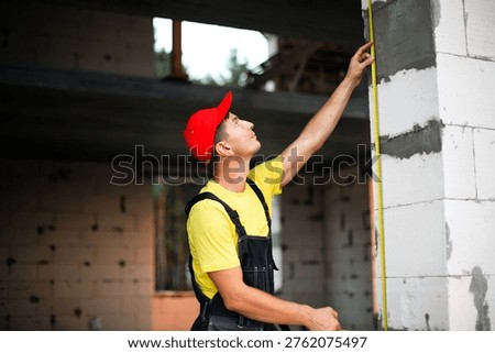 Construction worker checks vertical height of window opening, site measurements for installation, planning wall partitions, building renovation tasks.