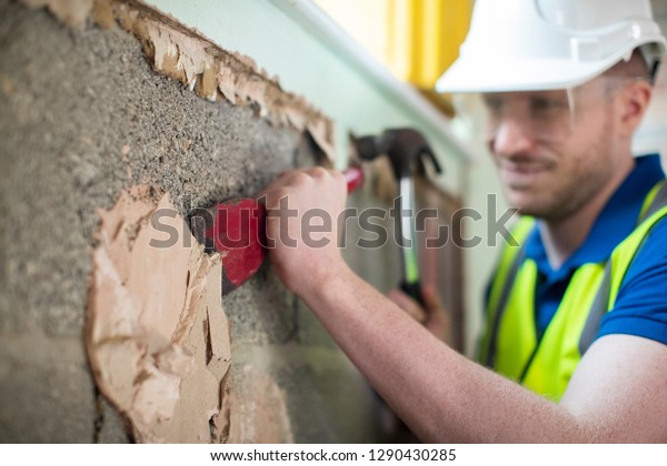Construction Worker With Chisel Removing Plaster\
From Wall In Renovated\
House