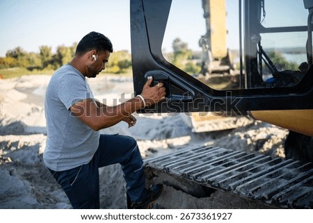 Construction worker climbing into the cabin of an excavator on a sandy construction site, ready to operate heavy machinery