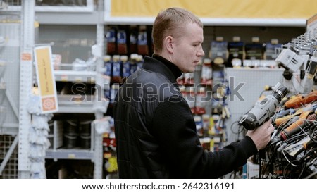 Construction worker comparing cordless drill features and prices while shopping in a hardware store, examining design and specifications. A man in a hardware store choosing a tool.