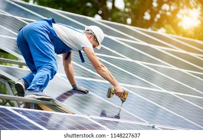Construction worker connecting photo voltaic panel to solar system using screwdriver on shiny surface and lit by sun green tree background. Alternative energy and financial investment concept. - Shutterstock ID 1148227637