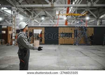 Construction worker coordinating operations using a walkie talkie inside a prefabricated house production facility