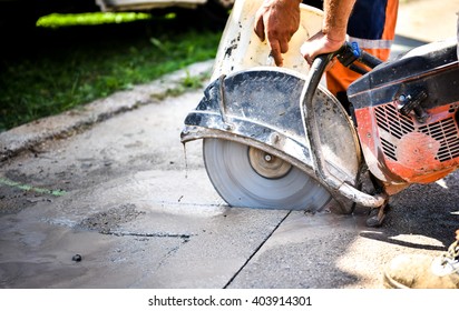 Construction worker cutting Asphalt paving stabs for sidewalk using a cut-off saw. Profile on the blade of an asphalt or concrete cutter with workers shoes and protective gear.
