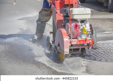 Construction worker cutting Asphalt paving stabs for sidewalk using a cut-off saw. Profile on the blade of an asphalt or concrete cutter with workers shoes and protective gear.
