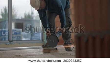 Construction worker cutting concrete with angle grinder, generating sparks, safety helmet, focused on task, indoor building process, handling heavy machinery with caution