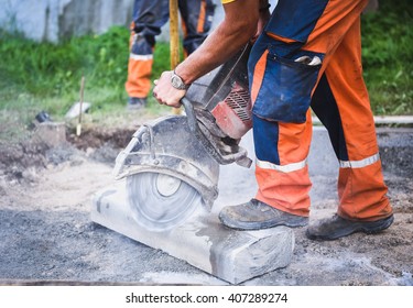 Construction worker cutting concrete paving stabs or metal for sidewalk using a cut-off saw. Profile on the blade of an asphalt or concrete cutter with workers shoes and protective gear.