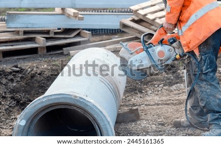 Construction worker cutting concrete pipe for drainage using a cut-off saw. Cutting concrete with a diamond blade creating cloud of silica dust
