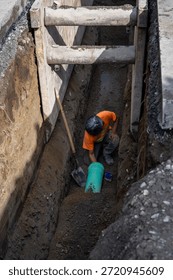 Construction worker in deep trench protected by Trench Box, coffin, while installing new 8 inch sewer line pipe under the road, building out infrastructure for new housing development
