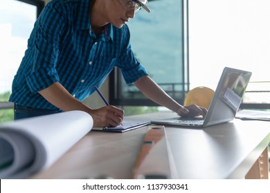 Construction Worker Or Designer Reviewing Construction Blueprint Or Drawing On Table At Construction Site Or Office.