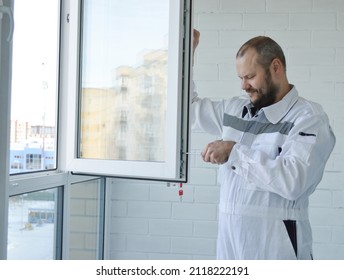 Construction Worker Dressed In A White Jumpsuit Repairing Plastic Window With Screwdriver Indoors. Installation Of Child Safety Locks On Windows.