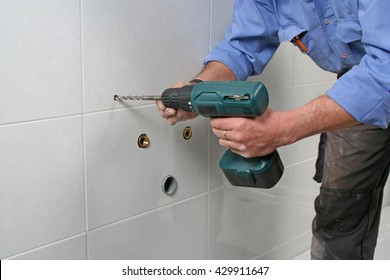 Construction worker drilling holes in the bathroom wall to install a sink.