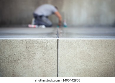 Construction worker filling the gap between the just glued ceramic tiles.