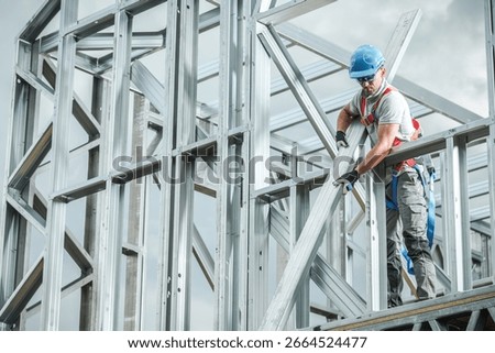 A construction worker is focused on assembling metal framework at a building site under clear skies. Safety gear is notably worn during this task.