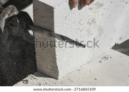 Construction worker focused on cutting autoclaved aerated concrete block with hand saw for building wall at site displaying professional workmanship