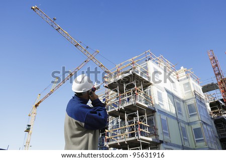construction worker, giant cranes, scaffolding and building-site in background. early morning shot