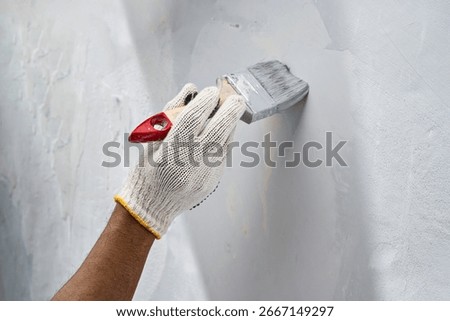 Construction worker in gloves using a paintbrush to apply paint to a wall during home renovation. Home renovation project