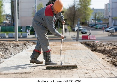 Construction Worker Grouting Dry Sand With Brush Into Paver Bricks Joints During Road Works