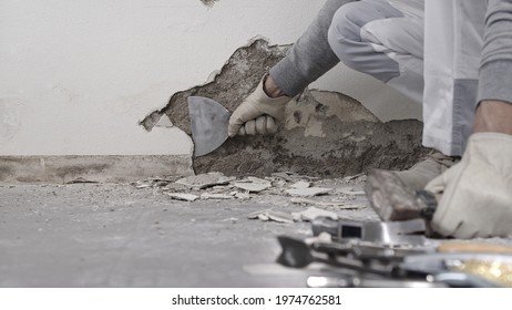 Construction worker hands with gloves working with spatula scrape off the plaster from the wall for house renovation, close up with rubble and tools - Shutterstock ID 1974762581