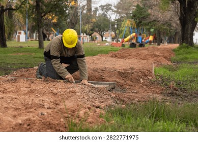 Construction worker with hard hat checking ground level using spirit level and straightedge in public park